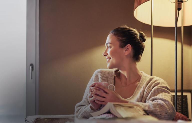 La donna è seduta comodamente con una tazza sotto una calda lampada incandescente
