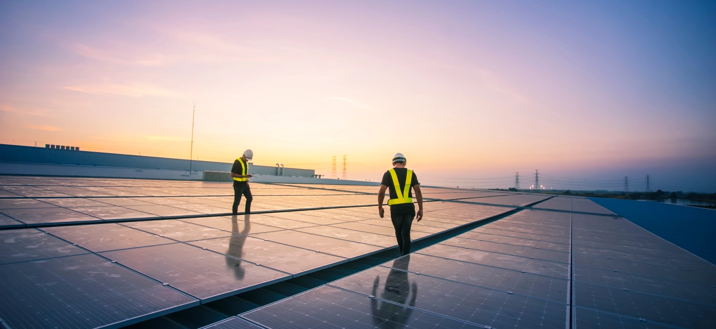 Zwei Installateure arbeiten an einem großen Solarfeld bei Sonnenaufgang.