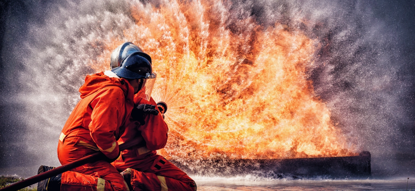 Zwei Feuerwehrleute löschen ein großes Feuer, das von einem Stromspeicher ausgeht.