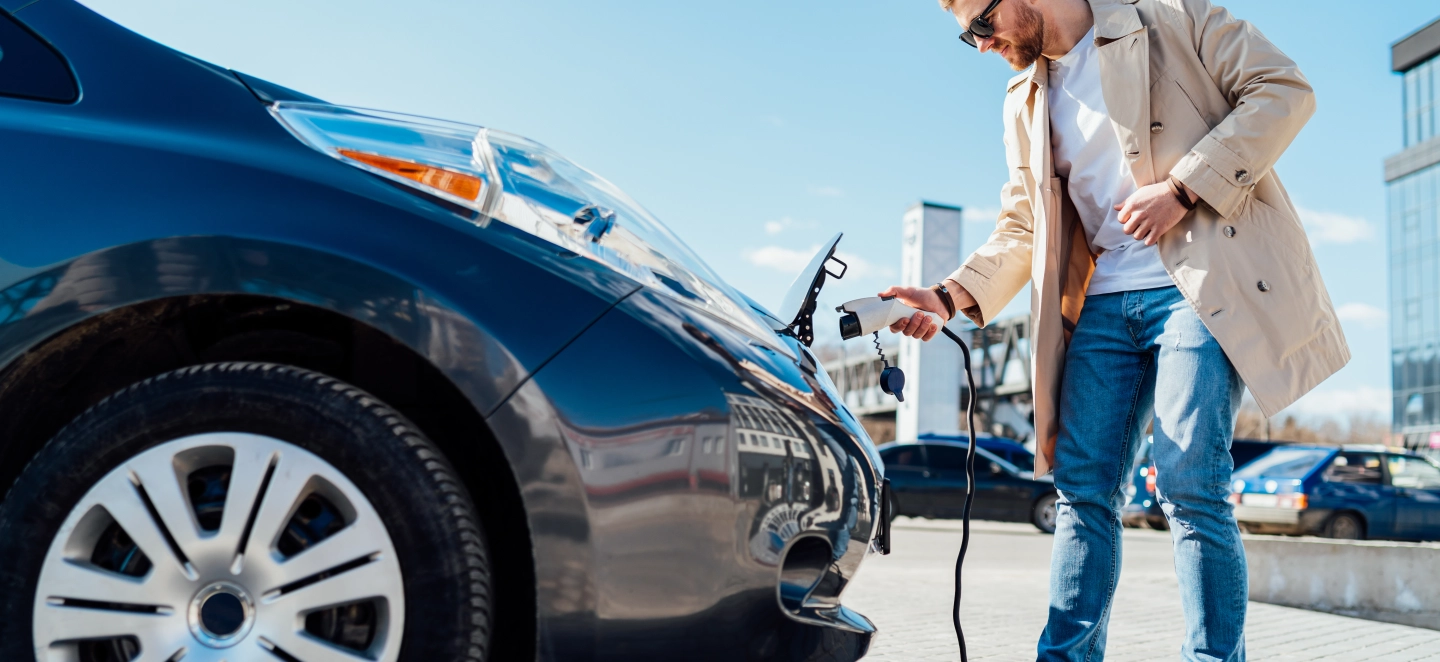 Junger Mann mit Sonnenbrille steckt das Ladekabel in sein Elektroauto.
