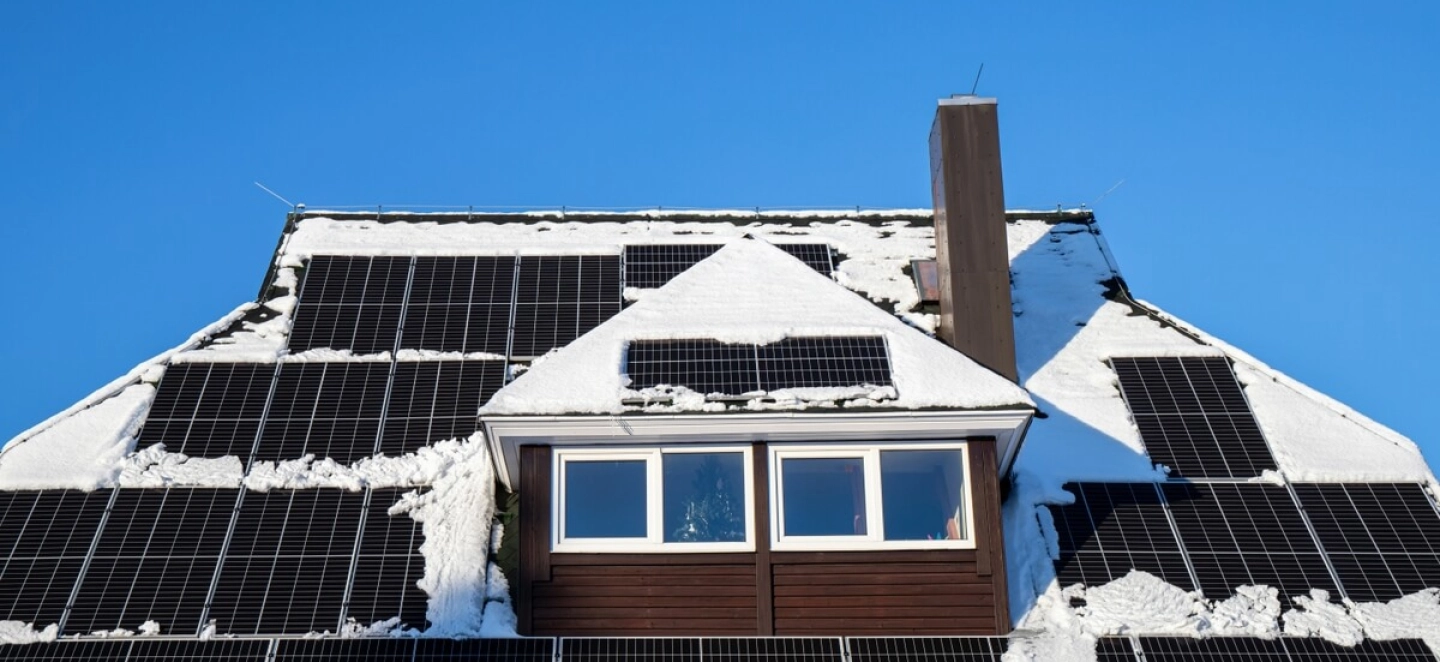 Eingeschneites Haus mit Solardach bei blauem Himmel im Winter. 