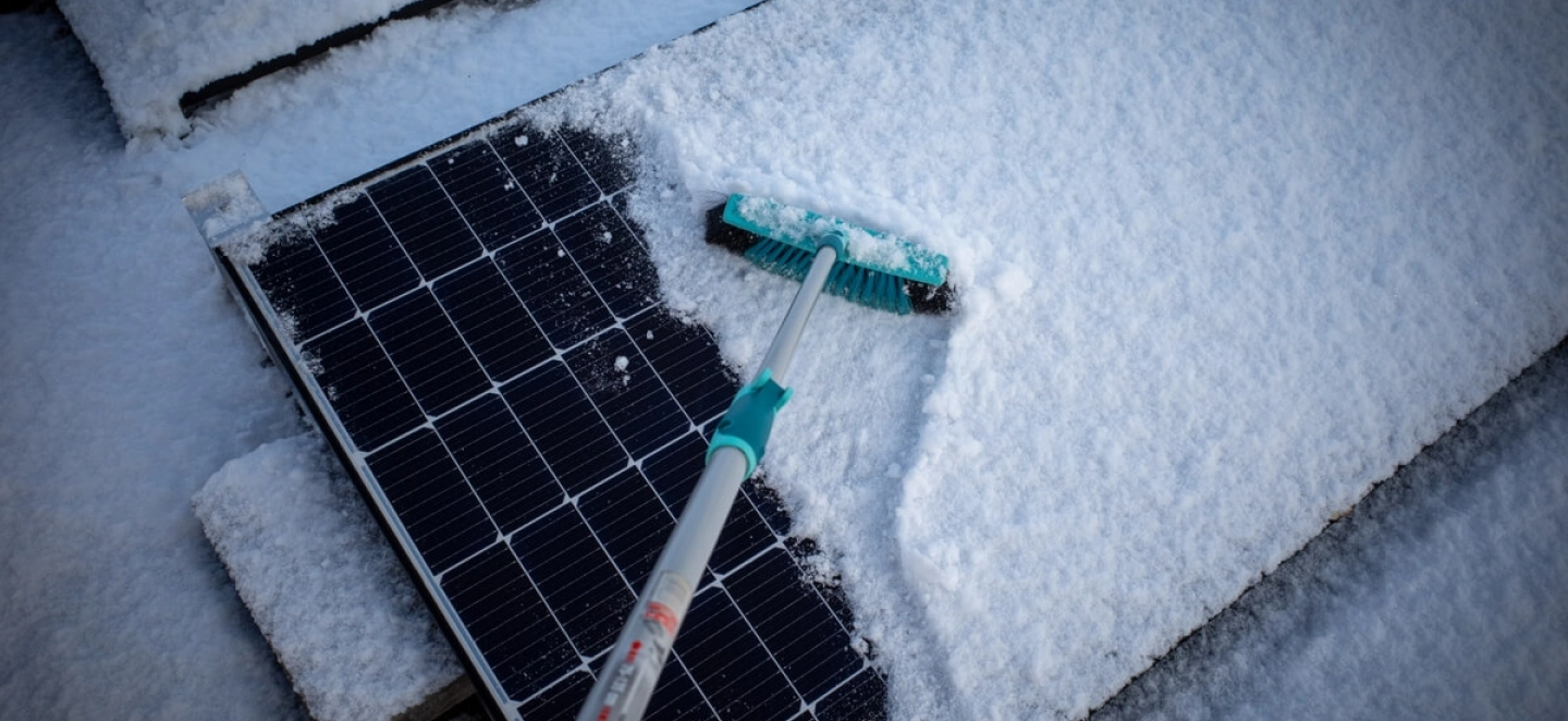 Schneebedeckte Solarmodule werden von einem Besen von Schnee befreit, sodass sie Strom erzeugen können.