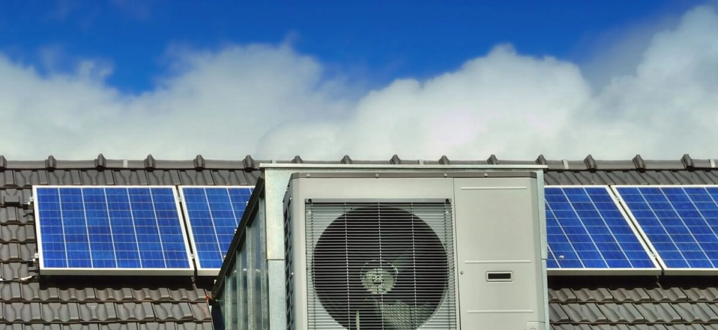 Im Vordergrund steht eine Wärmepumpe und im Hintergrund ist eine Photovoltaikanlage auf dem Dach zu sehen.