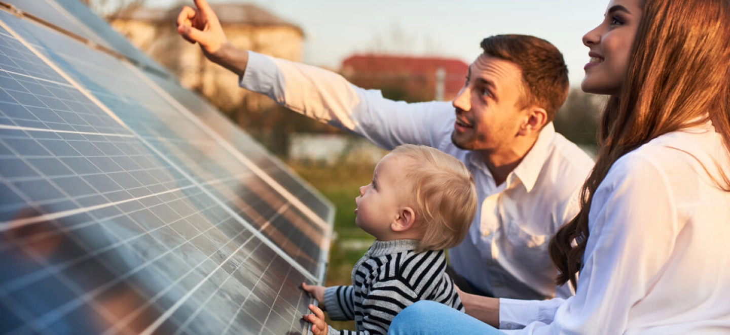 Ein junger Vater zeigt seinem Kind und seiner Frau eine Solarstrom-Anlage und erklärt die Speicherung.