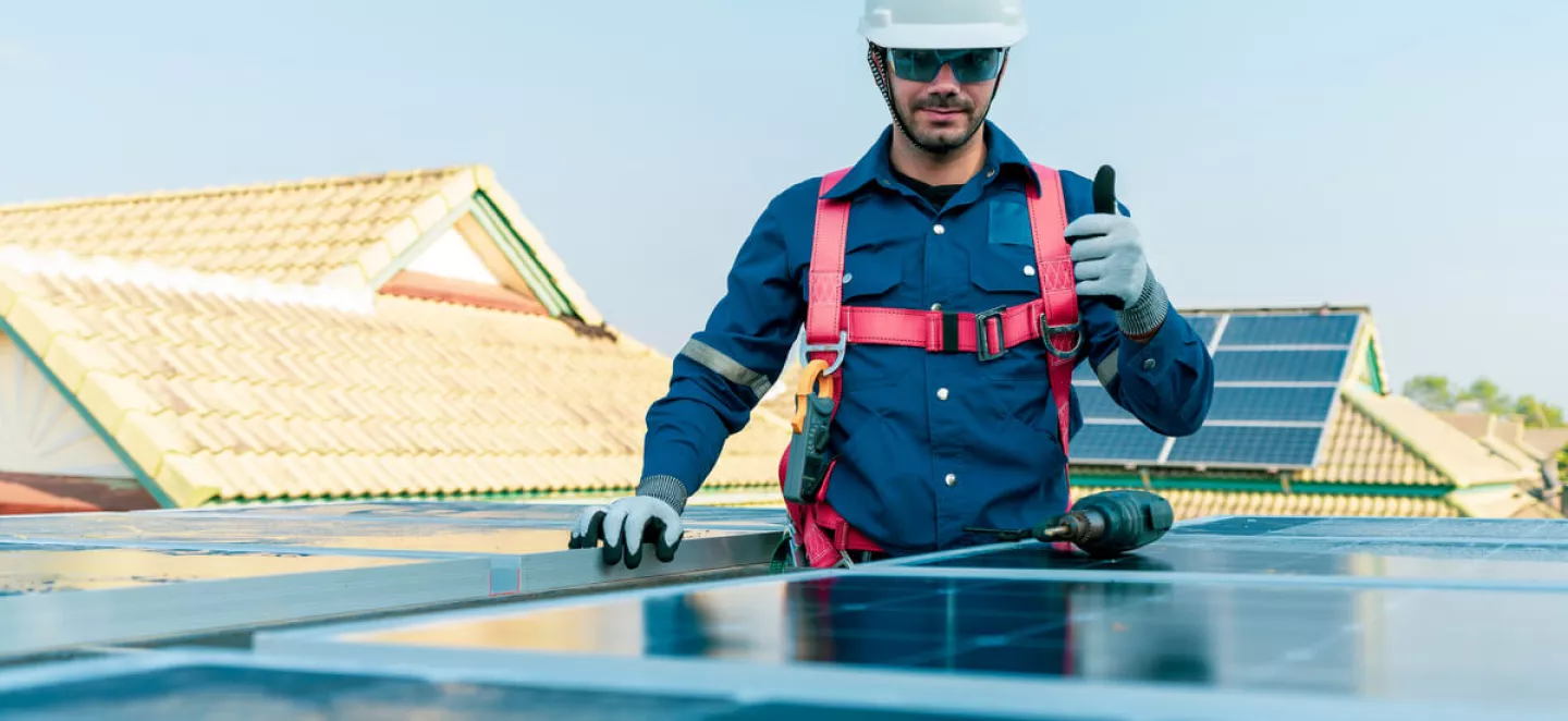 Ein Solar-Installateur steht auf dem Dach neben einer PV-Anlage und zeigt Daumen nach oben.