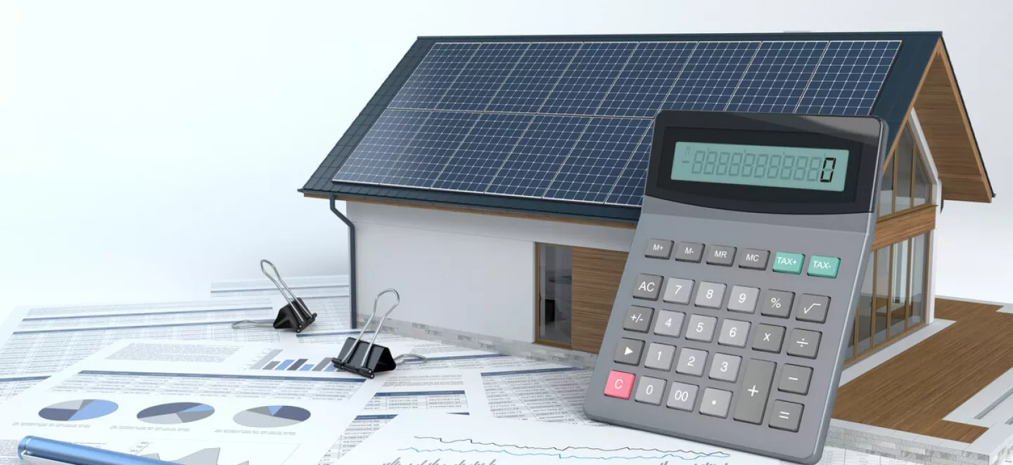 Das Modell eines Hauses mit Solardach mit Taschenrechner und vielen Zetteln mit Diagrammen zur PV-Regelung.