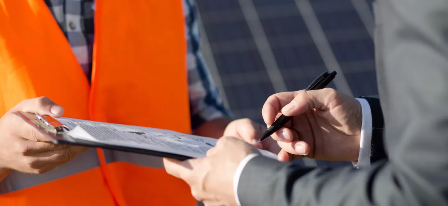 Ein Mann unterschreibt die Anmeldung seiner PV-Anlage, während ihm ein Installateur gegenübersteht.