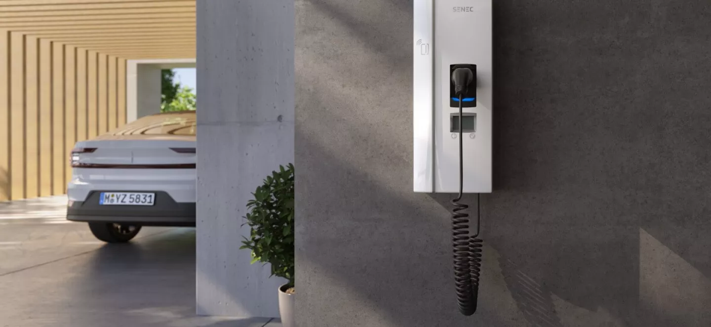 Wallbox hängt nach der Anmeldung im Carport bereit zum Laden des E-Autos, das im Hintergrund parkt.