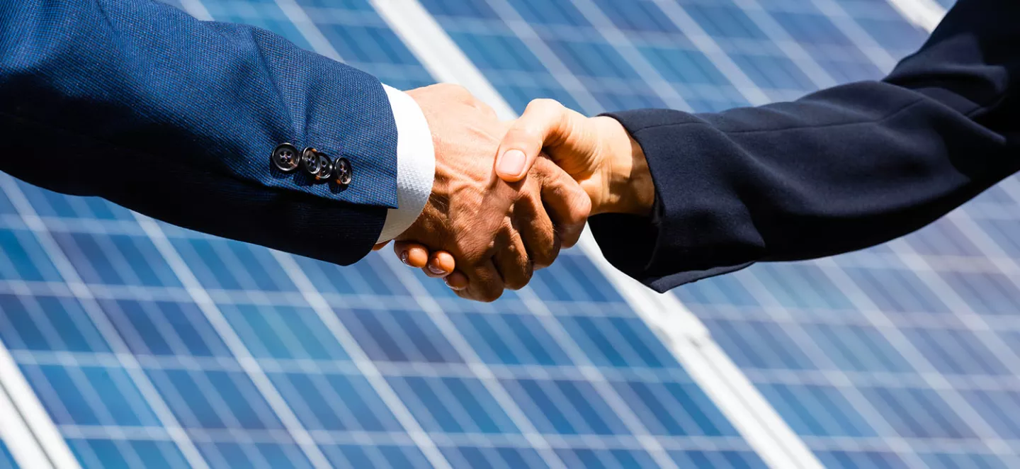 stretta di mano tra due businessman con pannelli fotovoltaici sullo sfondo