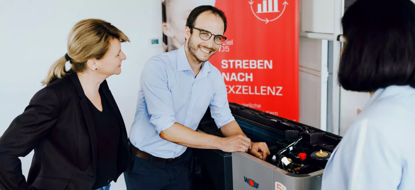 Ein Berater erklärt zwei Damen die Förderungen und Zuschüsse für Wärmepumpen direkt vor einem Gerät.