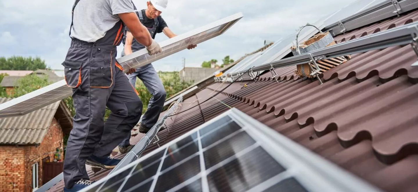 Zwei Solar-Installateure bauen PV-Module auf ein Dach.