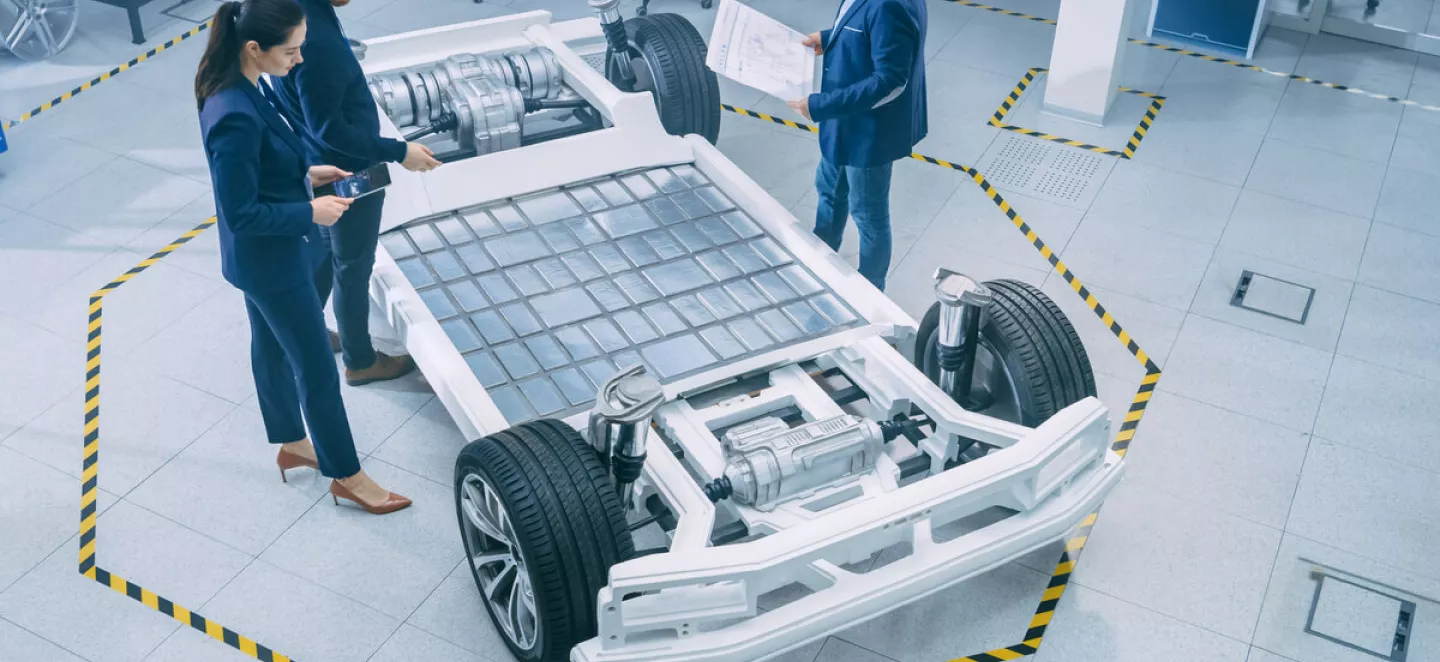 Wissenschaftler stehen um ein Chassis eines Elektroautos herum und begutachten die offen liegenden Batterien, die das E-Auto zu einem mobilen Stromspeicher machen.