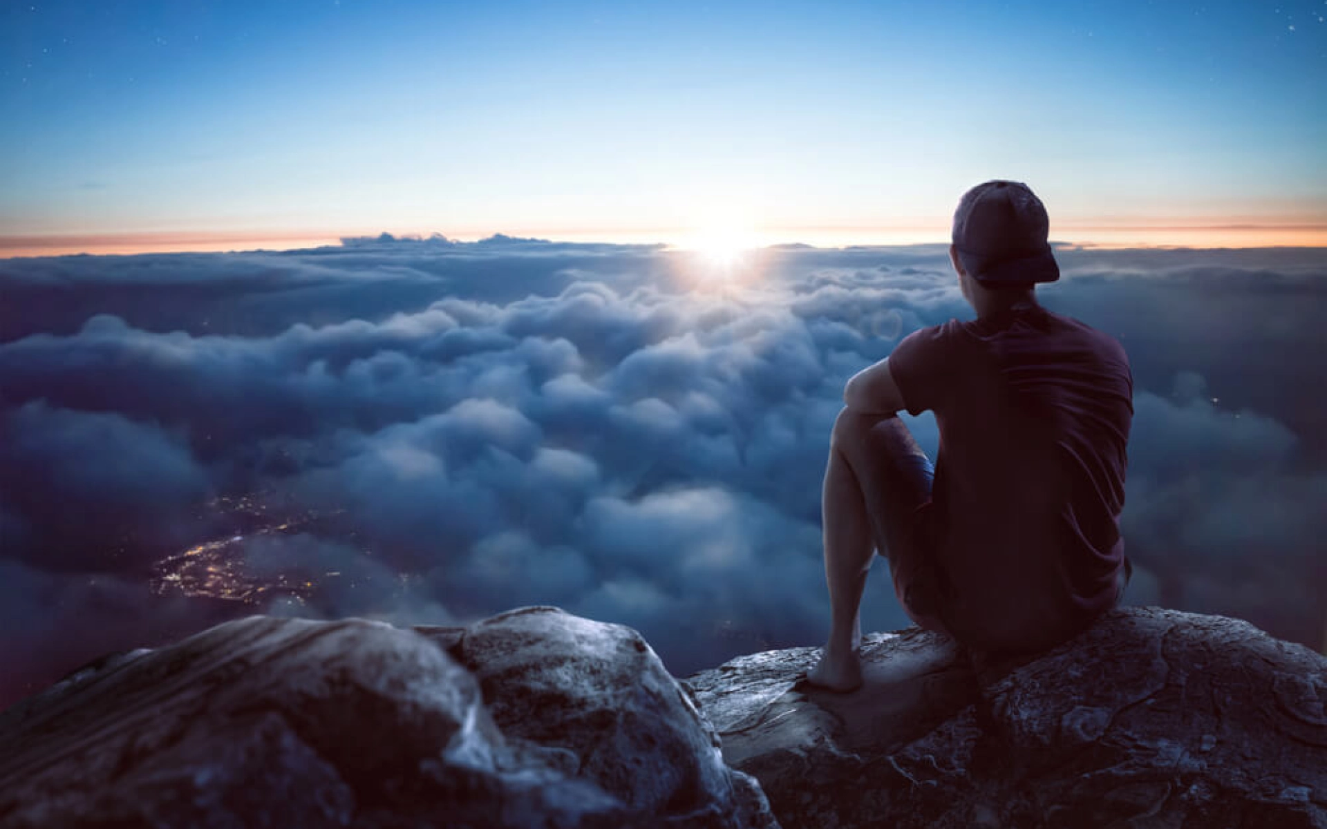 Ein Mann sitzt über den Wolken und schaut in das wolkige Tal während am Horizont die Sonne untergeht.