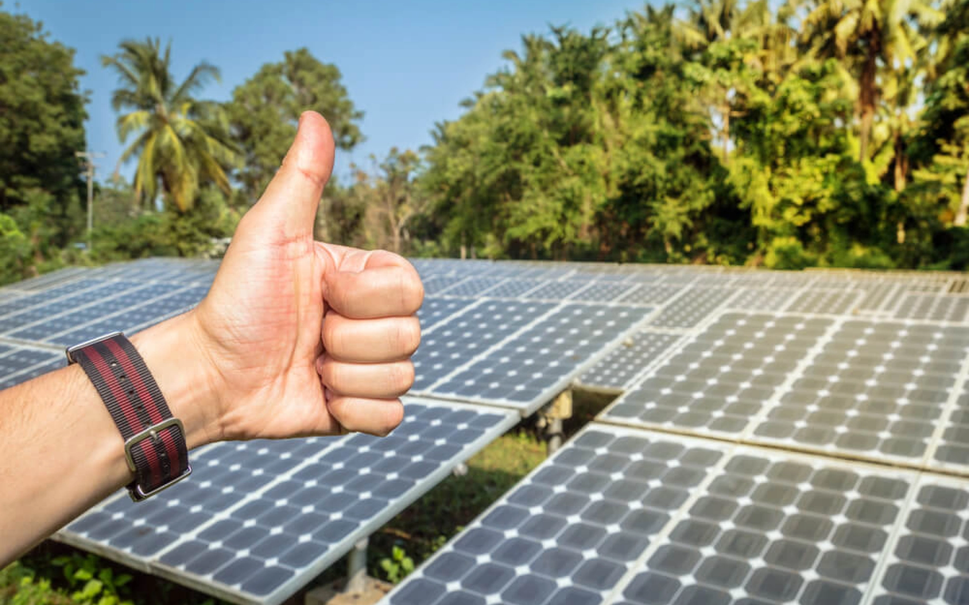Eine Hand zeigt Daumen nach oben und im Hintergrund ist eine Solaranlage zu sehen.