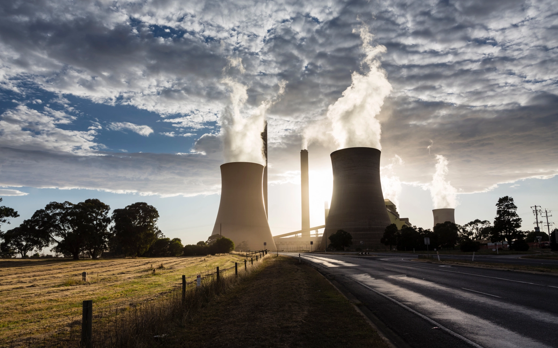 Zwei rauchende Schornsteine von einem Kohlekraftwerk im Sonnenuntergang. Das Bild symbolisiert das nahe Ende von fossilen Energieträgern und einem Umdenken. 