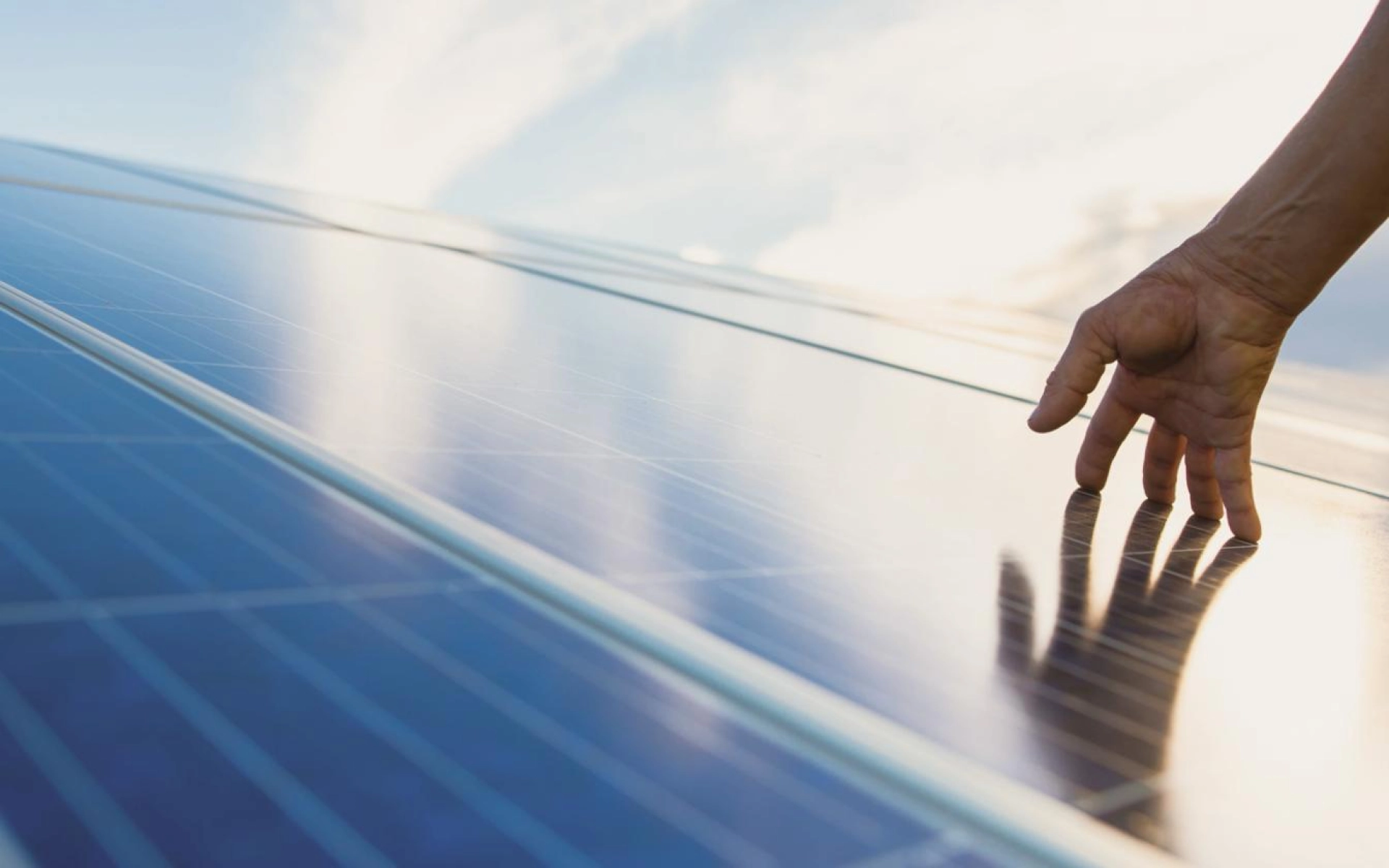 Eine Hand streicht über ein modernes Solarpanel, das frisch auf einem Dach installiert ist. 