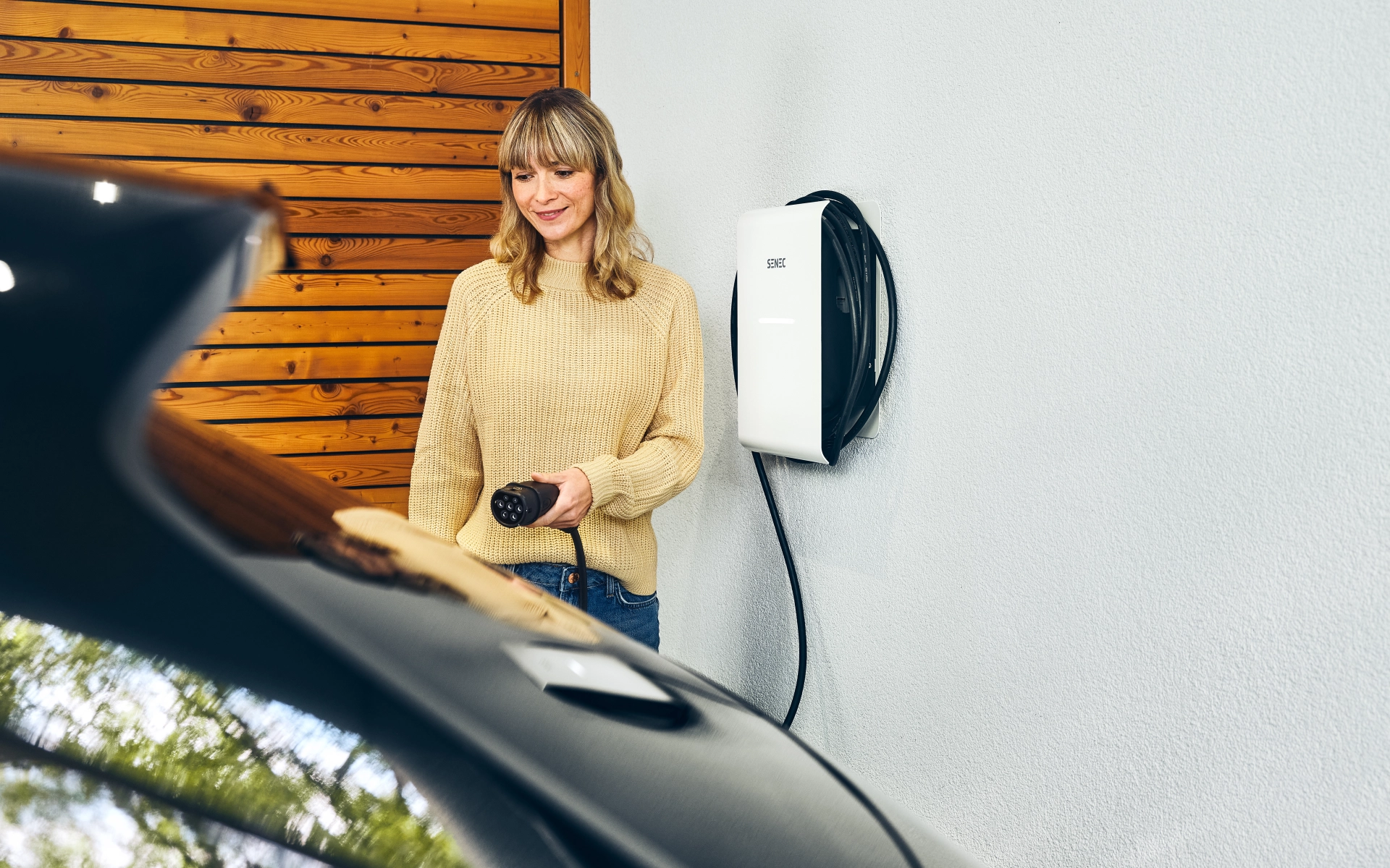 Junge Frau lädt ihr Elektroauto in der Garage zuhause.