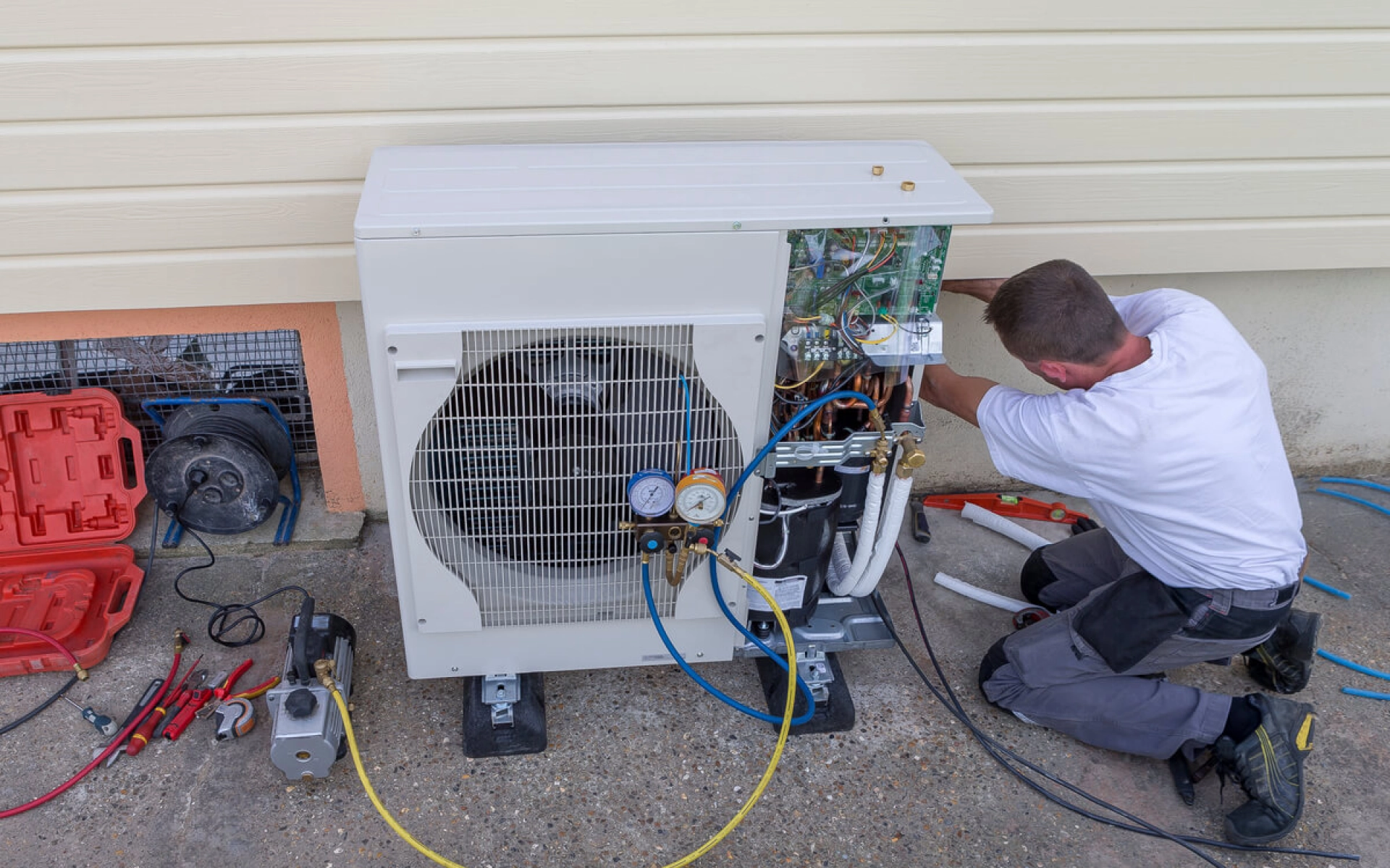 Ein Installateur schraubt an einer Wärmepumpe an der Seite von einem Haus.