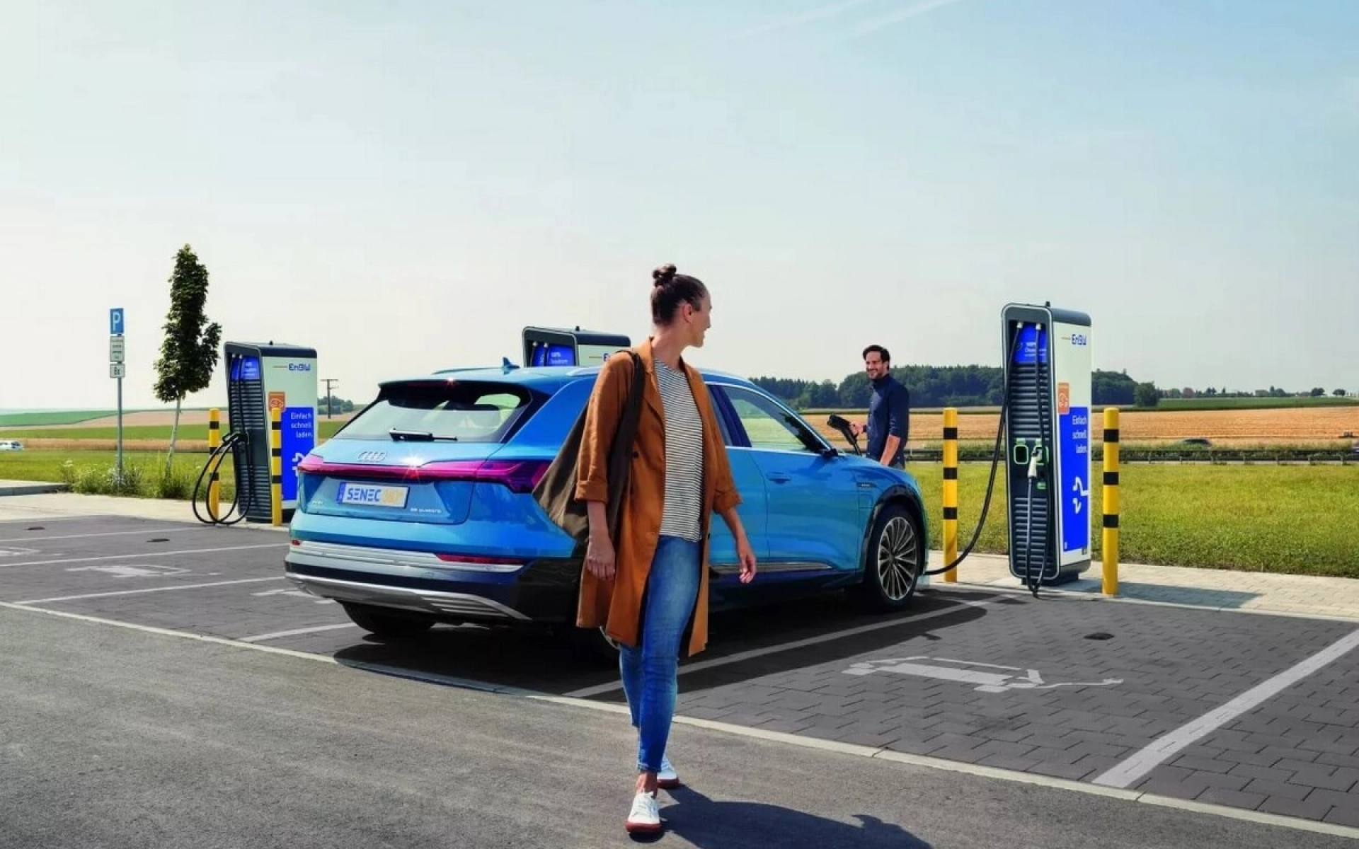 Eine junge Frau schaut sich nach ihrem neuen E-Auto um, während es mit Strom beladen wird.