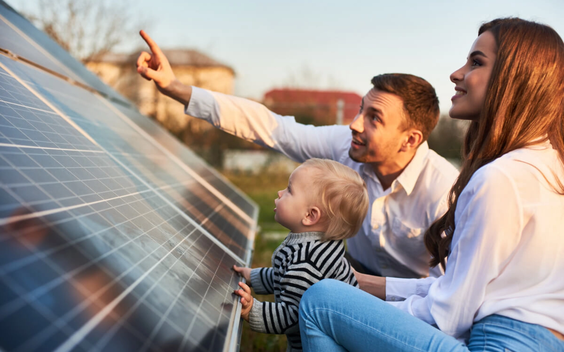 Ein junger Vater zeigt seiner jungen Frau und seinem kleinen Kind das Solardach ihres Hauses.