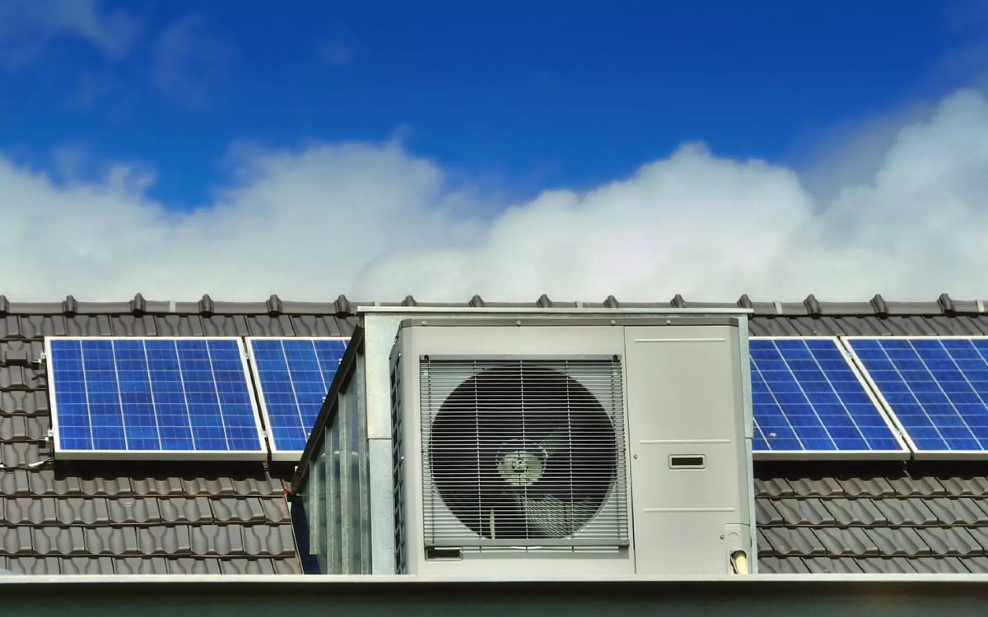Im Vordergrund steht eine Wärmepumpe und im Hintergrund ist eine Photovoltaikanlage auf dem Dach zu sehen.