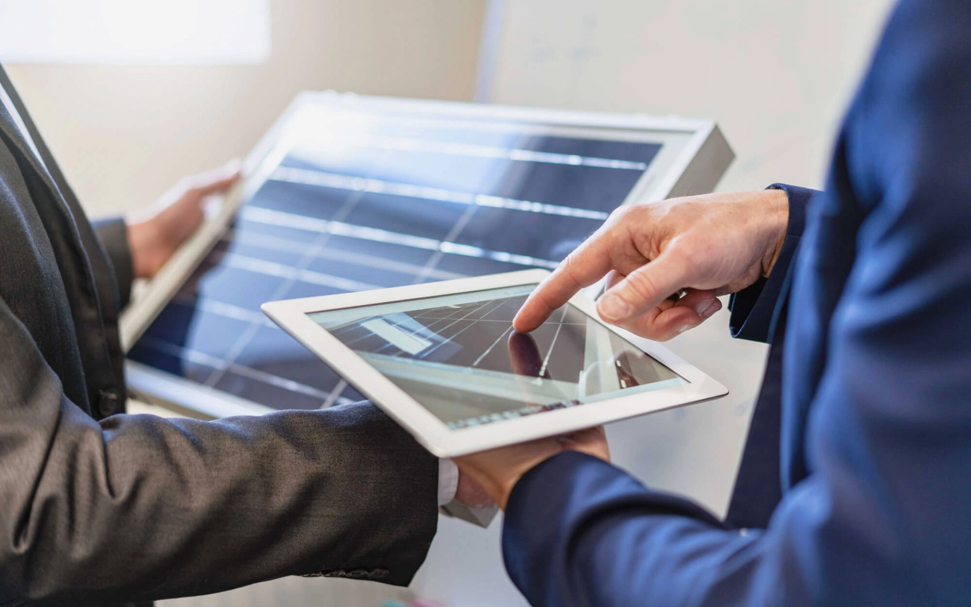 Zwei Hände im Hintergrund halten ein Solar-Panel und zwei Hände im Vordergrund berechnen auf einem Tablet die benötigte Leistung.