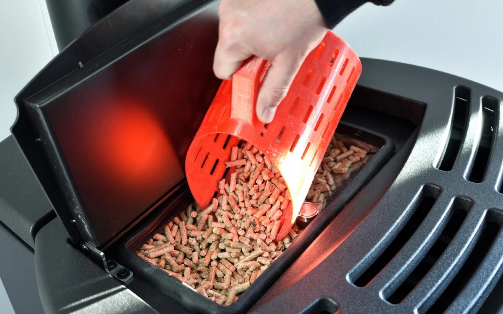 Eine Hand füllt mit einer Schaufel eine Pellet-Heizung mit Pellets.