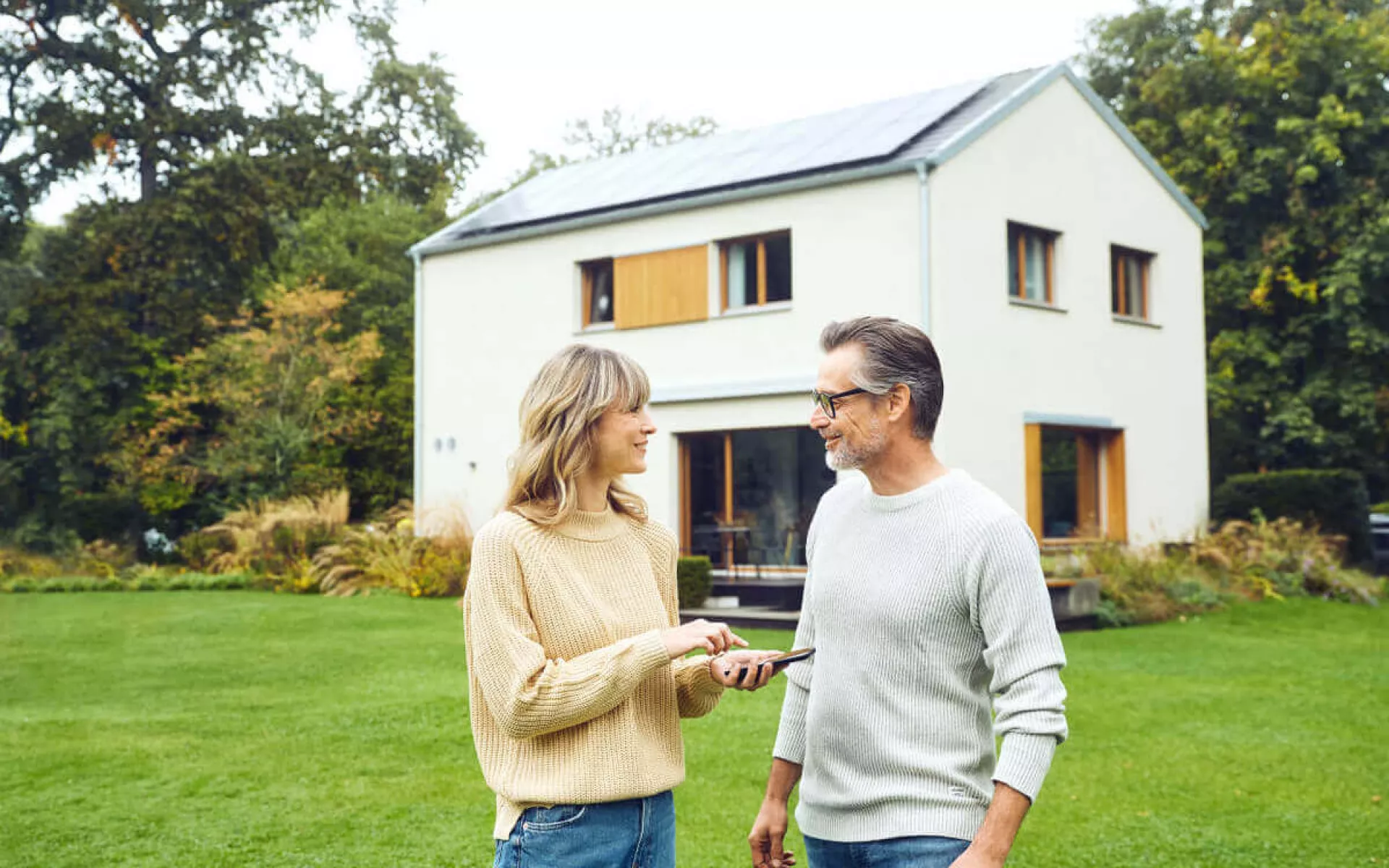 Eine Ehepaar im Gespräch und lachend. Im Hintergrund steht ihr Haus mit einer Solaranlage. 