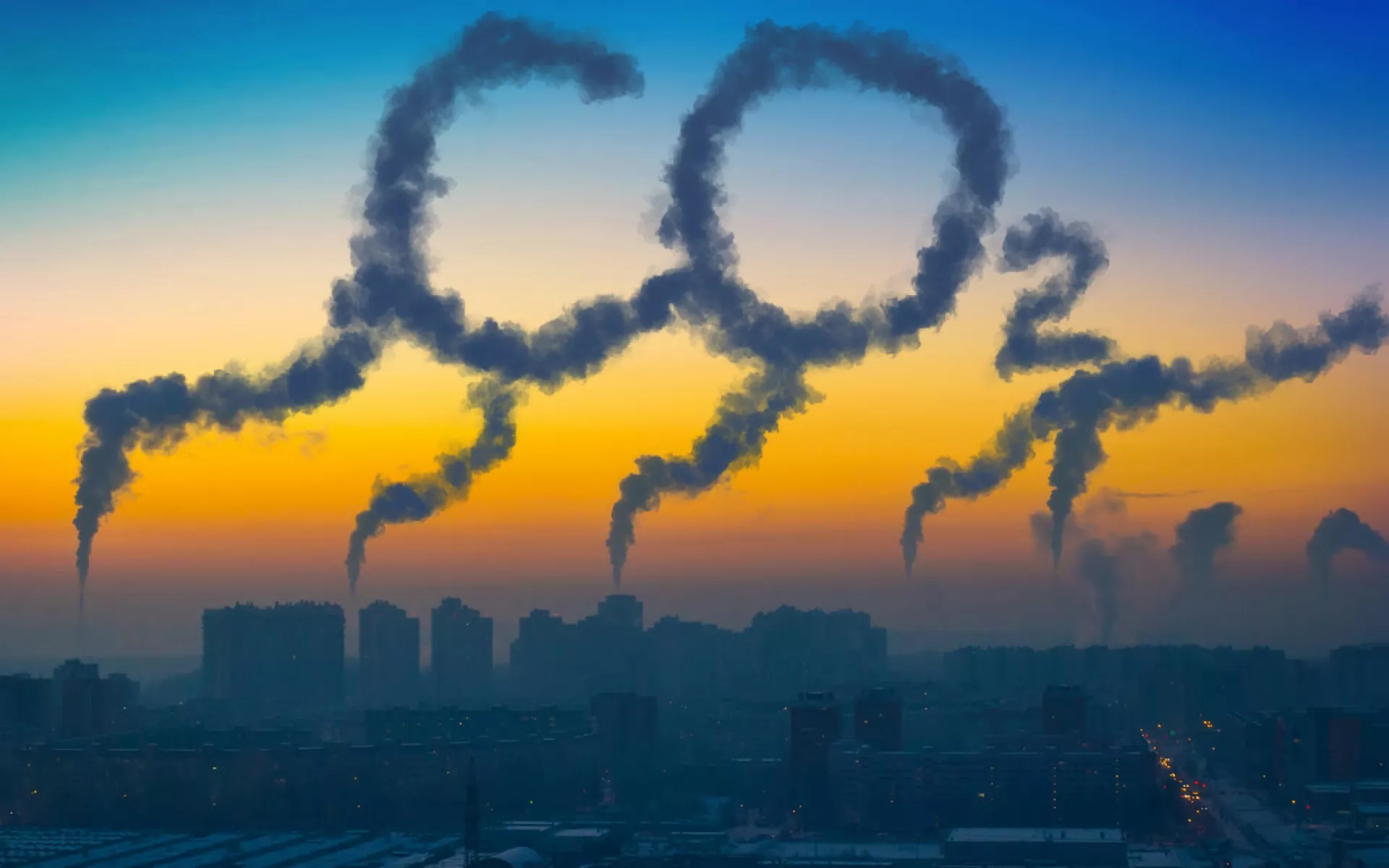 Die Skyline einer Stadt mit aufsteigendem Qualm aus Schornsteinen. Der Qualm zeichnet den Schriftzug CO2 in den Himmel.