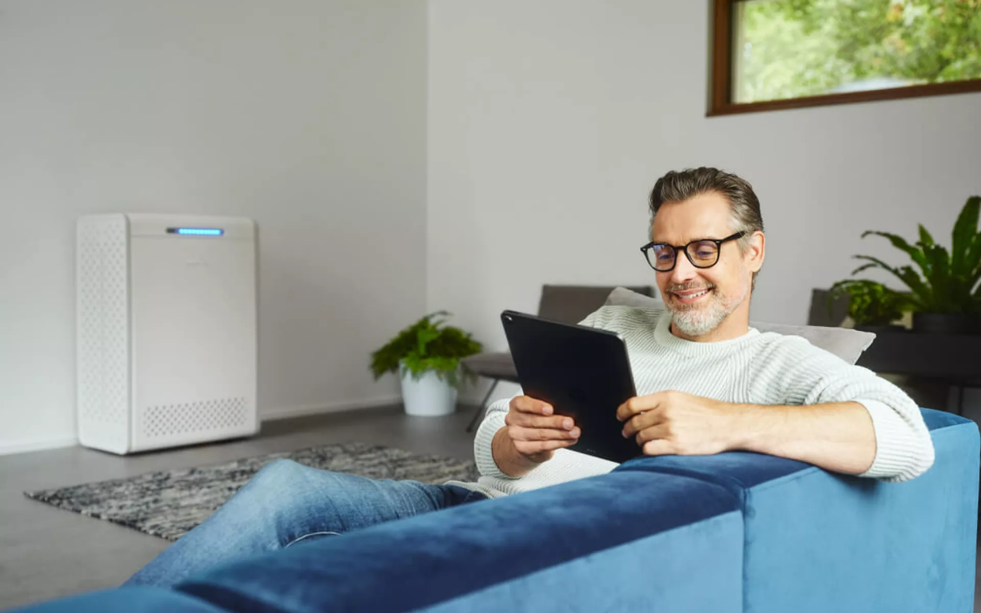 Ein Mann sitzt auf dem Sofa und steuert sein Home Energy Management System per Tablet.