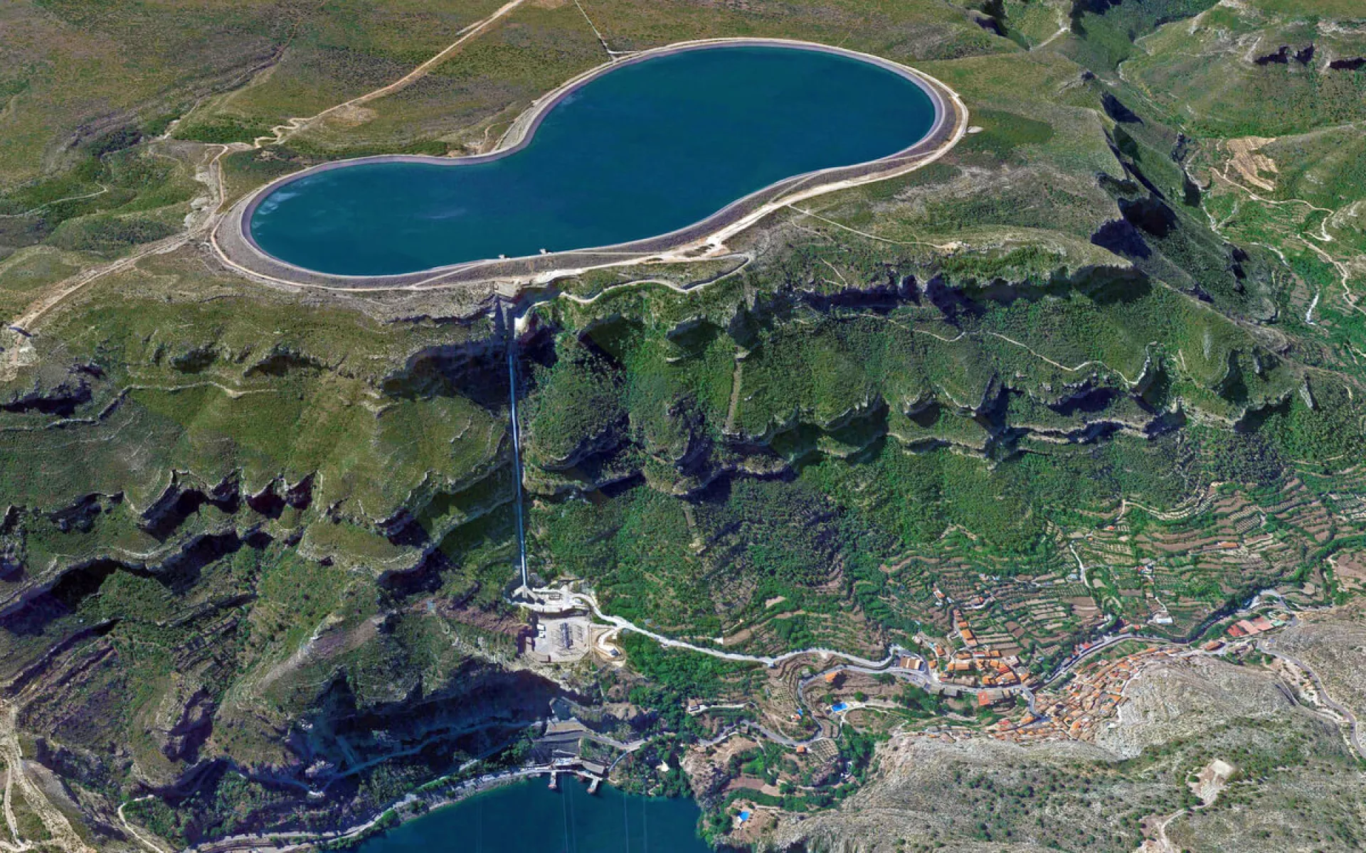 Ein großer See auf einer Hochebene mit einem angeschlossenen Wasser-Kraftwerk und einem Dorf im Tal.