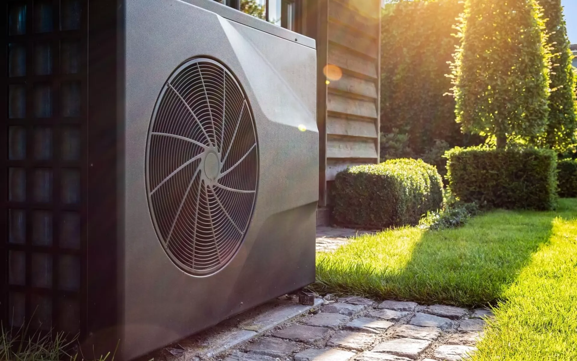 Eine Wärmepumpe vor dem Haus im Hintergrund der Garten.