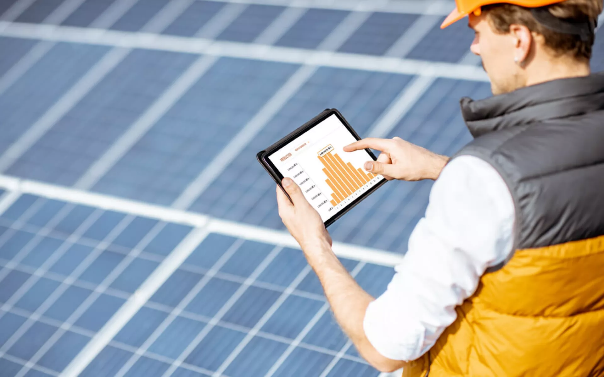Eine Solarinstallateur analysiert mit seinem Tablet und einer speziellen Software die Effektivität der Solaranlage im Hintegrund.