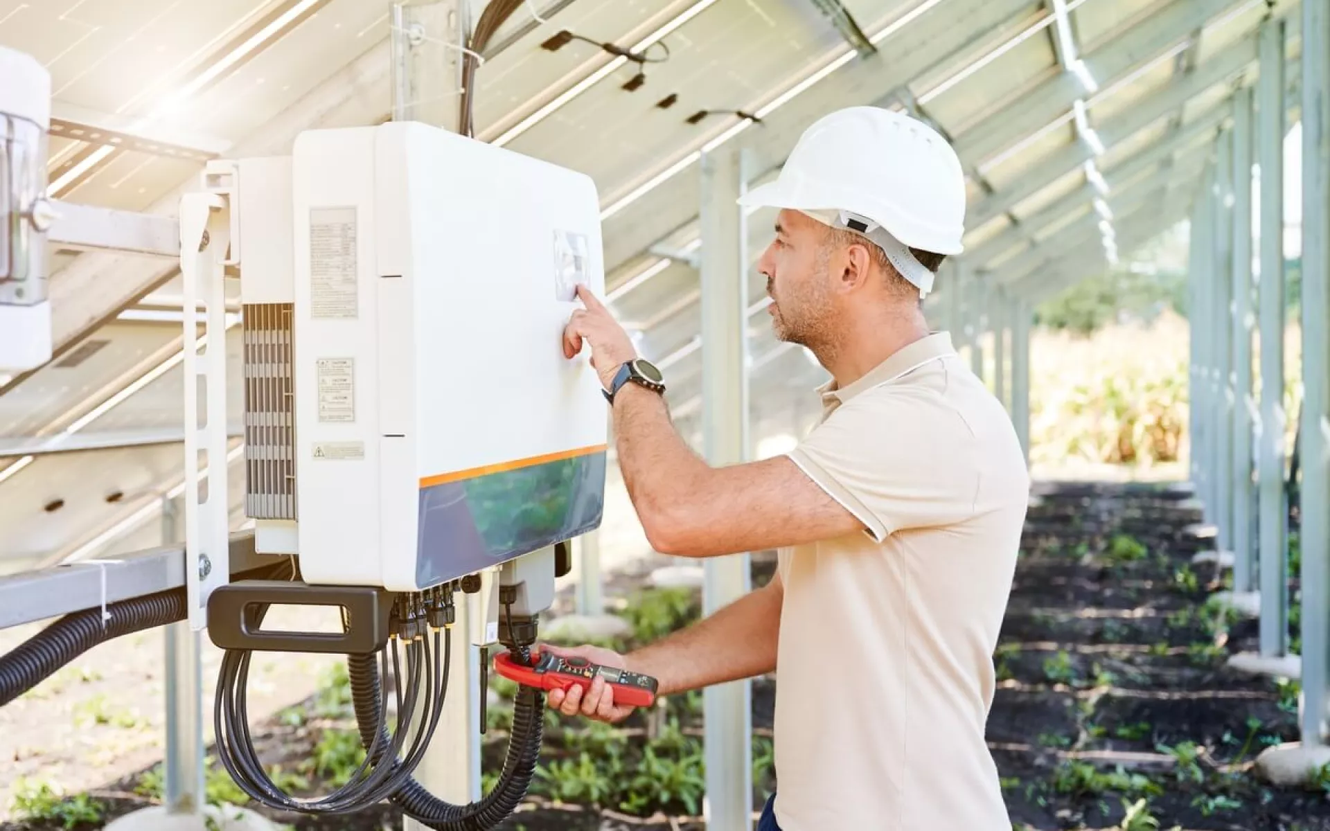 Ein Elektriker installiert einen Wechselrichter unterhalb einer Solar-Anlage.
