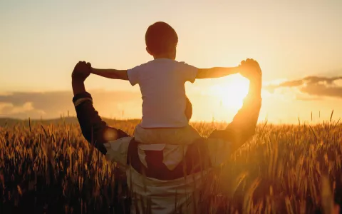 Vater mit Kind auf den Schultern bei Sonnenuntergang