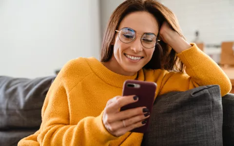 Frau sitzt lächelnd mit Smartphone auf der Couch