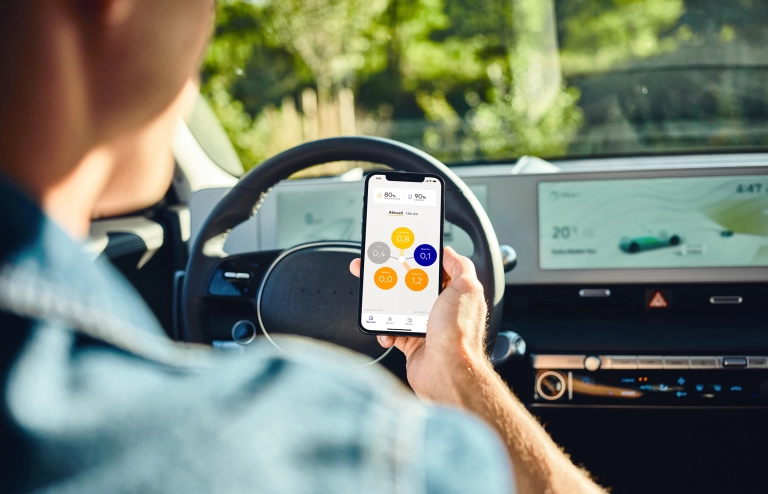 Persona che guida un'auto elettrica ed utilizza l'app SENEC.App con lo smartphone