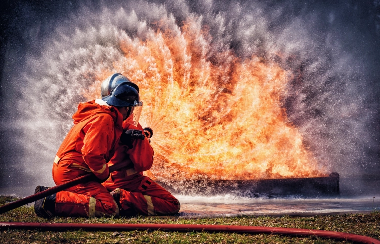 Zwei Feuerwehrleute löschen ein großes Feuer, das von einem Stromspeicher ausgeht.