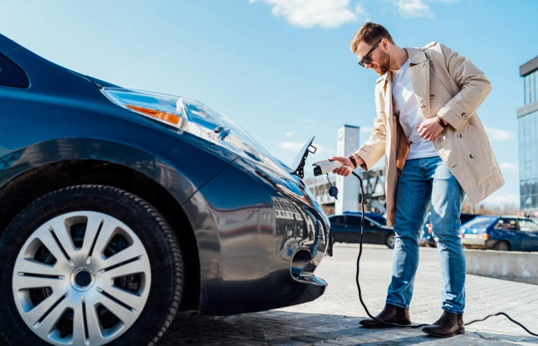 Junger Mann mit Sonnenbrille steckt das Ladekabel in sein Elektroauto.
