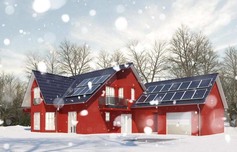 Ein Haus im Winter bei Schneefall und Kälte mit einer Photovoltaikanlage auf dem Dach zum Heizen.