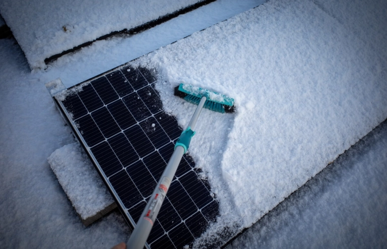 Schneebedeckte Solarmodule werden von einem Besen von Schnee befreit, sodass sie Strom erzeugen können.