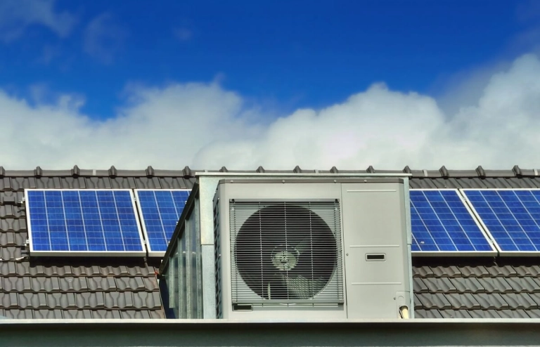 Im Vordergrund steht eine Wärmepumpe und im Hintergrund ist eine Photovoltaikanlage auf dem Dach zu sehen.