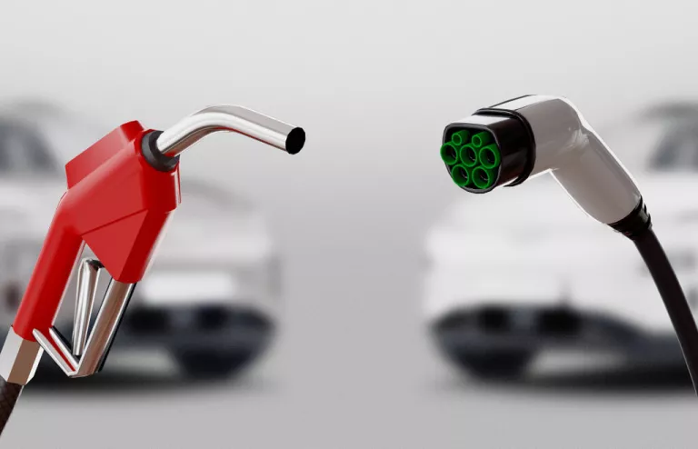 Rechts im Bild ist eine Ladepistole für ein Elektroauto. Links im Bild ist eine rote Zapfpistole für einen Benziner.