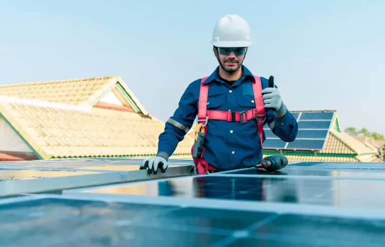 Ein Solar-Installateur steht auf dem Dach neben einer PV-Anlage und zeigt Daumen nach oben.