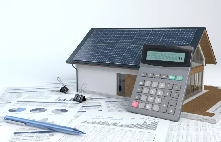 Das Modell eines Hauses mit Solardach mit Taschenrechner und vielen Zetteln mit Diagrammen zur PV-Regelung.