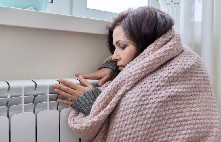 Eine junge Frau sitzt mit dicker Decke an der kalten Gasheizung. 