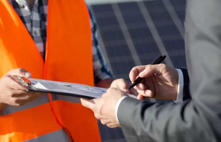Ein Mann unterschreibt die Anmeldung seiner PV-Anlage, während ihm ein Installateur gegenübersteht.