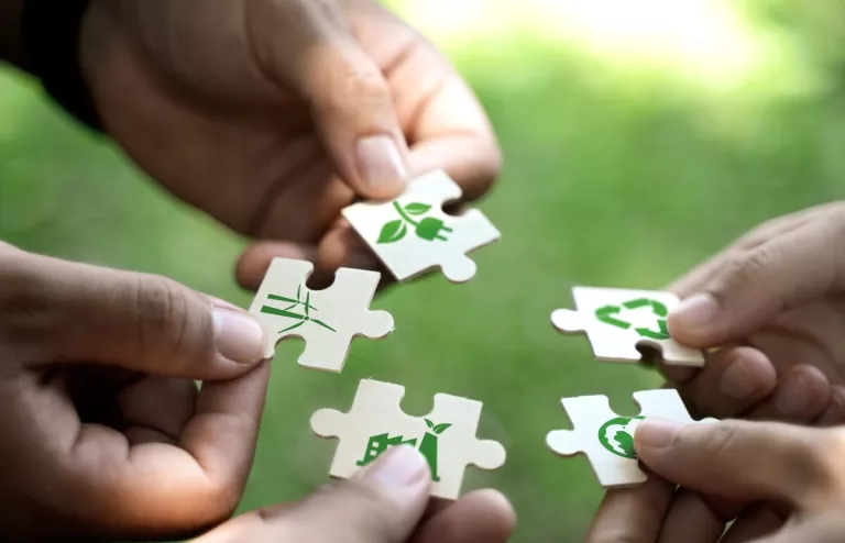 Fünf menschliche Hände führen fünf Puzzlestücke zusammen, auf denen Symbole für die erneuerbaren Energien aufgedruckt sind.