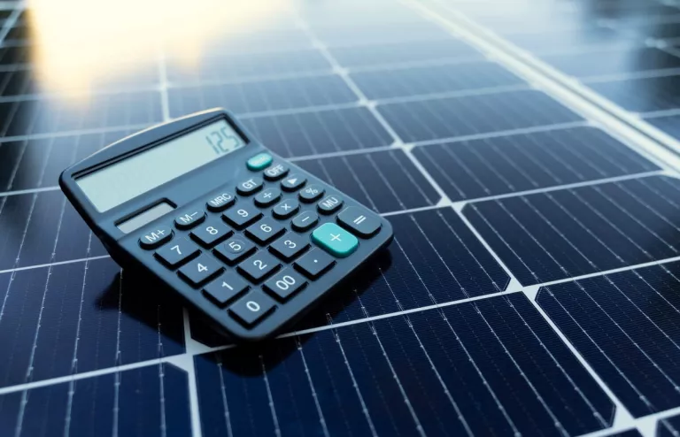 Auf einem Solar-Panel liegt ein Taschenrechner, um die Größe der Photovoltaikanlage zu berechnen.