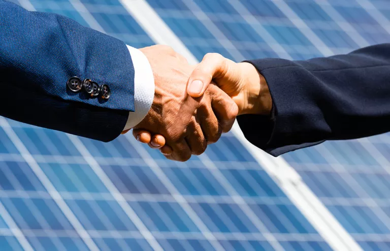 stretta di mano tra due businessman con pannelli fotovoltaici sullo sfondo